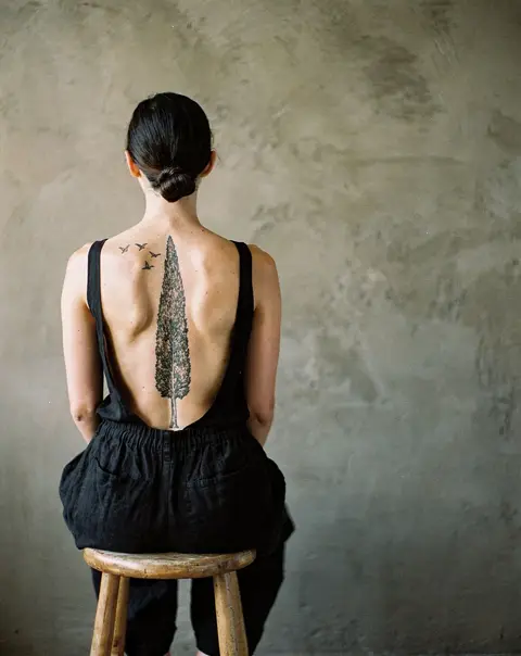 A tall cypress tree with birds along a woman's spine