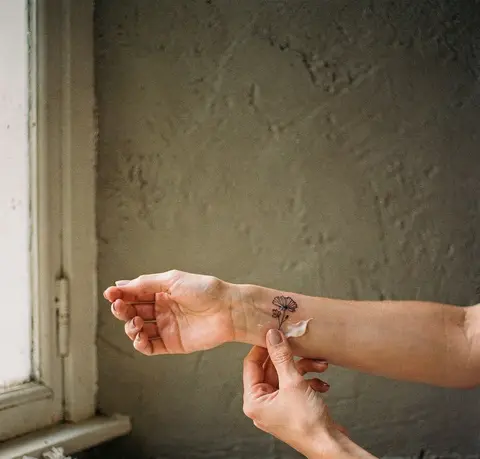 Fingers putting a thin layer of balm on a small flower tattoo